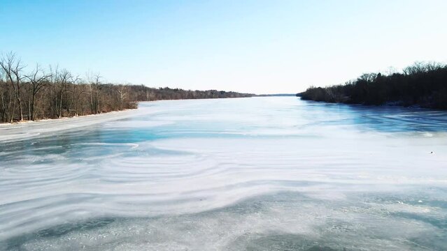 A low aerial flight over a frozen river showing patterns of water flow in the ice as you pass over at a relativly high speed.