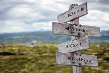 kind words cost nothing text quote engraved on wooden signpost outdoors in nature.