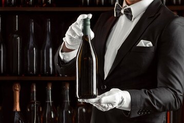 Elegant waiter sommelier wine steward with a bottle of wine. Examination of wine products. Restaurant staff among shelves of wine bottles. Stylish middle-aged man with a grey beard.