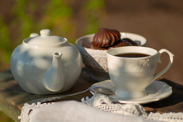 Elegant cup, lace tablecloth, teapot, marshmallow in chocolate, wooden table. Outdoor breakfast, picnic, brunch, spring mood. Soft focus