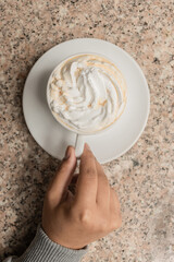 delicious cup of coffee with cream, details of the hands holding the cup on a textured table, lifestyle and drink in studio, energy