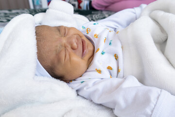 details of a newborn crying, she wears a hat, gloves and is lying down warm with a blanket, latin baby lifestyle, face details