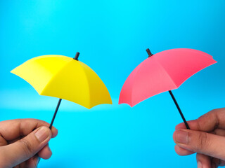Hand holding two umbrella on blue background.