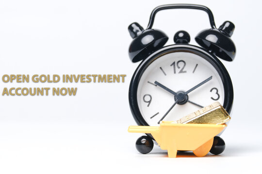 Selective focus picture of miniature goldbar own wheelbarrow, alarm clock insight and word open gold investment account now.
