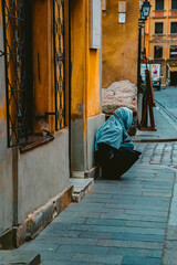 Fototapeta premium Woman with Headscarf Crouched on Sidewalk of Yellow Buildings