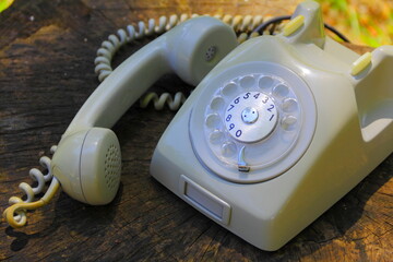 Vintage telephone. Retro beige rotary phone over wooden surface with sunset lights.