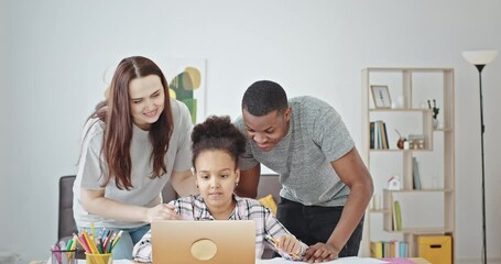 Diverse parents supporting daughter during online lesson. Happy multiracial father and mother smiling and gesturing thumb up while supporting cheerful mixed race daughter fulfilling assignment on