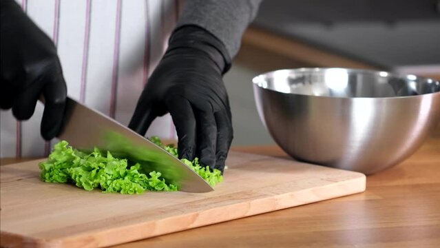 Close up of hands cutting romaine lettuce on a wooden cutting board and adding it to a bowl. Cook hands chopping green salad lettuce leaves. Preparing vegetarian salad. Keto or paleo diet