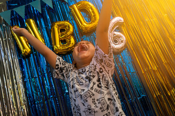 Happy Latin boy with his arms outstretched in the air in front of the decoration for his sixth...