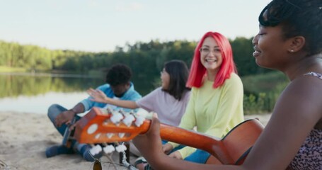 Friend's campfire in the open air, outside, beautiful girl plays guitar, the rest of the people listen, drink beer, sing talking, good atmosphere, time off from school, work, vacation
