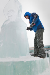 Portrait of a sculptor in a blue winter suit with a chisel in his hands on the scaffolding