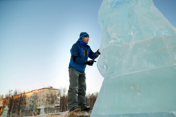 Portrait of a sculptor in a blue winter suit with a chisel in his hands on the scaffolding