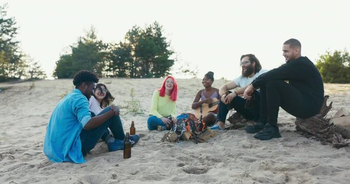 Friends from different countries erasmus came to study together they spend their free time from studying at common bonfire on beach by lake, drinking beer, talking, singing, joking, fooling around