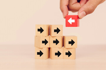 Close-up hand chooses arrow icon on cube wooden toy block stacked with pointing to opposite directions for way of adapting to change leader and transform concept.