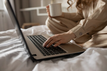 A girl in pajamas with a cup of coffee in the morning prints on a laptop, close-up.