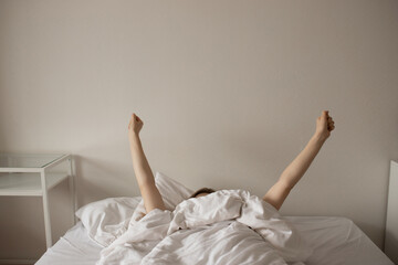 A young girl stretches in bed in the morning.
