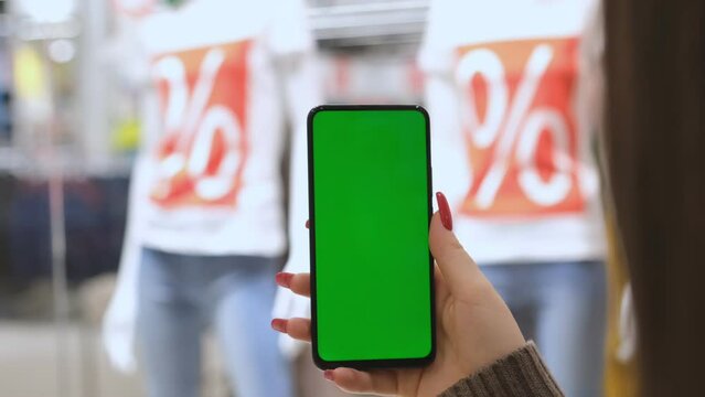 Big discounts. Big sale. Lots of discount coupons to save money on your smartphone. A girl is holding a phone with a green screen in a shopping center. black Friday. green screen. sale.