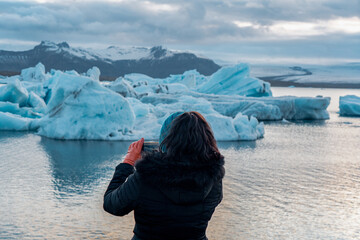 Woman with Orange Gloves Takes Picture of Glacier Chunks in Jokulsarlon Glacier Lagoon in Iceland