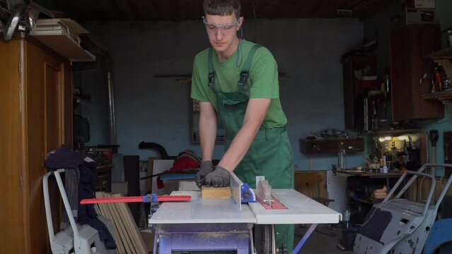 Carpenter in protective gloves and glasses plans a wooden blank on a woodworking machine in his home workshop. The process of making furniture with your own hands. 