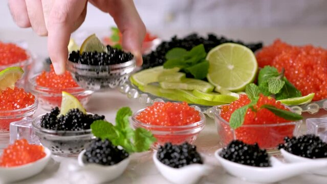 Tasting red salmon caviar and black beluga sturgeon salted roe. Hands pick caviar in bowl. Set of delicious snacks on banquet, close up. Expensive delicacy, serving. Bowls with red and black caviar
