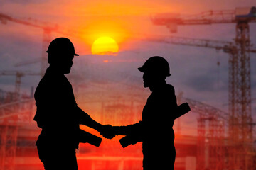 Silhouettes of male and female engineers shake hands to demonstrate cooperation with supervisors on construction site plans at sunset.