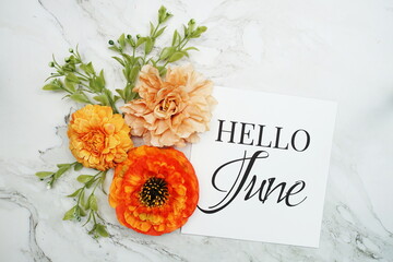 Hello June text with orange flower bouquet on marble background