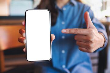 Mockup image of a young woman holding, showing and pointing finger at a mobile phone with blank...