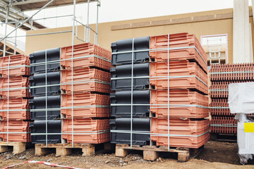 Alternating pallets of red and black roofing tiles on site