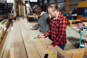 Carpenter in a woodworking factory measuring a plank