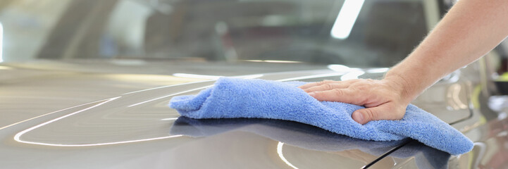 Hood of gray car is wiped with microfiber at car wash