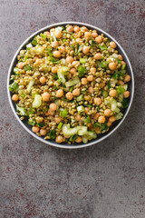 Vegetarian freekeh salad with chickpeas, celery and herbs close-up in a plate on the table. Vertical top view from above