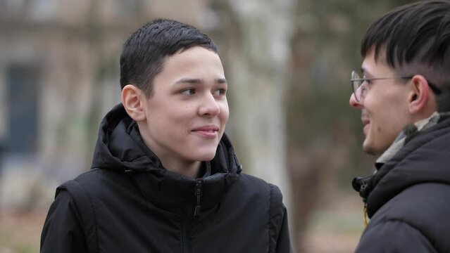 A 13-year-old boy and a young guy are standing on the street and talking. Shallow depth of field, close-up
