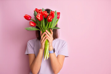 International Women's Day. a happy woman in a purple T-shirt hides her face behind a bouquet of spring tulip flowers that she holds in her hands. Space for text. Very peri