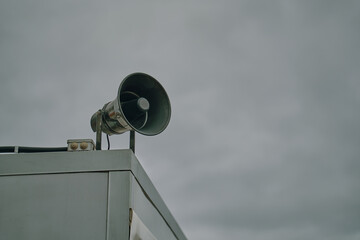 Megaphone on cloudy sky background. Emergency alert siren. City hazard warning system. Providing security in town, notification of emergencies. Copy space for text.