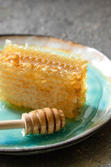 Sealed honeycomb of honey with wooden Honey Dipper for mixing and tasting natural honey on a blue porcelain plate on a white table