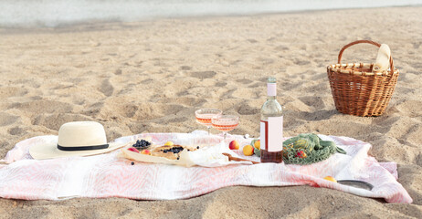Fototapeta na wymiar Beautiful summer picnic at sunset on beach with rose wine, cheese, blueberry galette and fresh fruits. Copy space