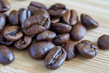 A bunch of roasted coffee beans in close-up on a wooden surface.