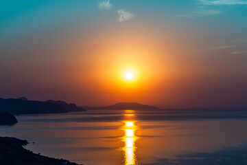 Beautiful amazing summer sunrise, bright orange colors. Cape of the mountain jutting into the sea and the reflection of the sun on the water