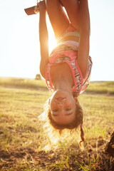 The girl is hanging upside down on a tree in summer in orange sunlight and a light dress. Summer...