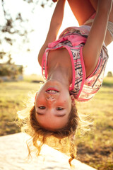 The girl is hanging upside down on a tree in summer in orange sunlight and a light dress. Summer...