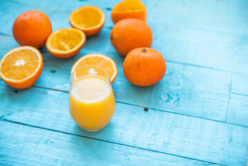 Glass of natural juice of several organic oranges, some whole, some squeezed, for the diet, on a blue wooden table. Healthy breakfast