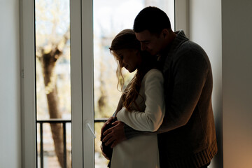 Beautiful pregnant woman and her handsome husband are hugging and smiling while spending time...