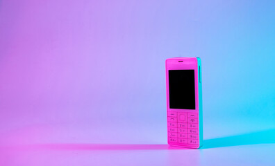 Neon phone vintage concept. Old classic analog mobile cellphone isolated on nostalgia neon pink blue background. Minimalism retro style concept. 80s.