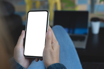 Cell phone mockup image blank white screen. Woman hand holding, using mobile phone during working on laptop computer at coffee shop.