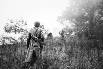 Single Re-enactor Dressed As German Wehrmacht Infantry Soldier In World War II Walking In Patrol Through Autumn Forest. WWII WW2 Times. Photo In Black And White Colors.