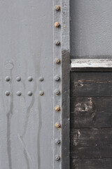 A close-up of metal plates and a wooden panel. The plates are attached with rivets and bolts.
