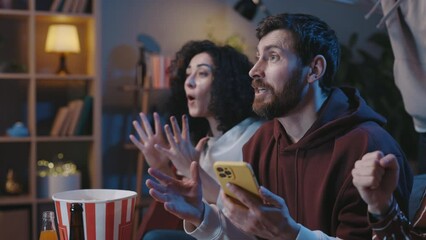 Enjoy favorite football club play. Soccer fans sitting on a couch and watching sports game on TV, while checking results at the smartphone at special app to online bet. Team wins championship concept.