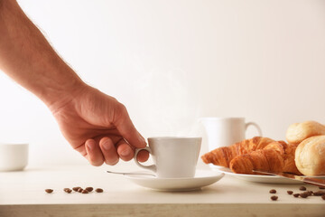 Hand taking hot morning coffee on breakfast table with croissants