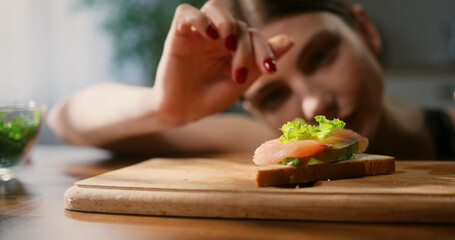 Close up of woman gently placing lettuce leaf onto salmon avocado toast. Healthy eating concept.