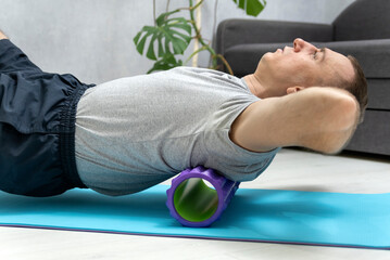 Man uses foam roller massager for relaxation and back pain. Workout at home. Man doing fascia exercise on the floor. Myofascial roller.